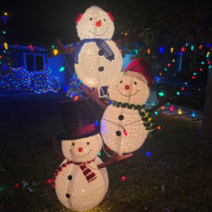 3 snowmen, one on top of another, outside in a yard.