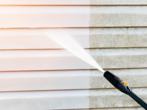 A person power washing the exterior of a house, removing dirt, grime and mildew to enhance the appearance and protect the siding