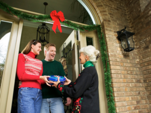 This is an image of an older woman giving a gift to a man and woman at their front door.