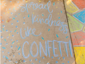 This is an image of the words "spread kindness like confetti" written with chalk on a sidewalk.