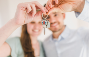 This is an image of a man and a woman holding a set ok keys on a keychain of a house with the word home on it.