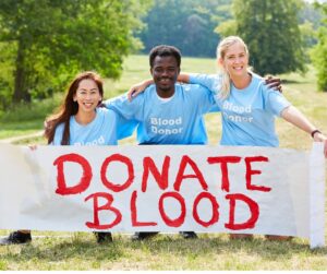 This is an image of 3 people holding a Donate Blood banner.