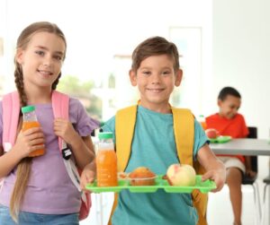 This is an image of a boys holding a school lunch tray and a girl holding bottle of juice.