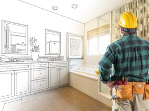 This is an image of a man wearing a hard hat and tool belt looking inside a bathroom where half the room is plans and the other half is real.