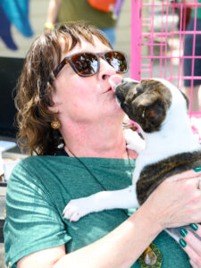 a woman in a green shirt holding a puppy with brown and white markings licking her face.