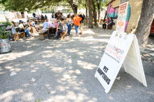 picnic tables with people talking and looking at dogs with a new hope animal rescue sign off to the side.