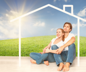 This is an image of a couple siting in front of a wooden outline of a house.