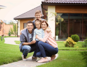 This is an image of a dad, mom and 2 kids hugging in front of a house.