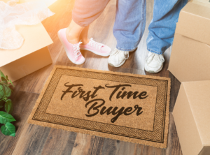 This is an image of a doormat that says First Time Buyer and 2 peoples legs in the background.