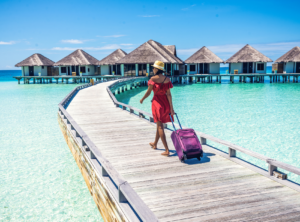 This is an image of a women pulling her suitcase behind her as she walks towards a resort.