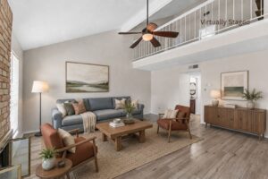 Virtually staged living room with vaulted ceiling, brick fireplace, ceiling fan, and open loft above at 2100 Kippling Drive.