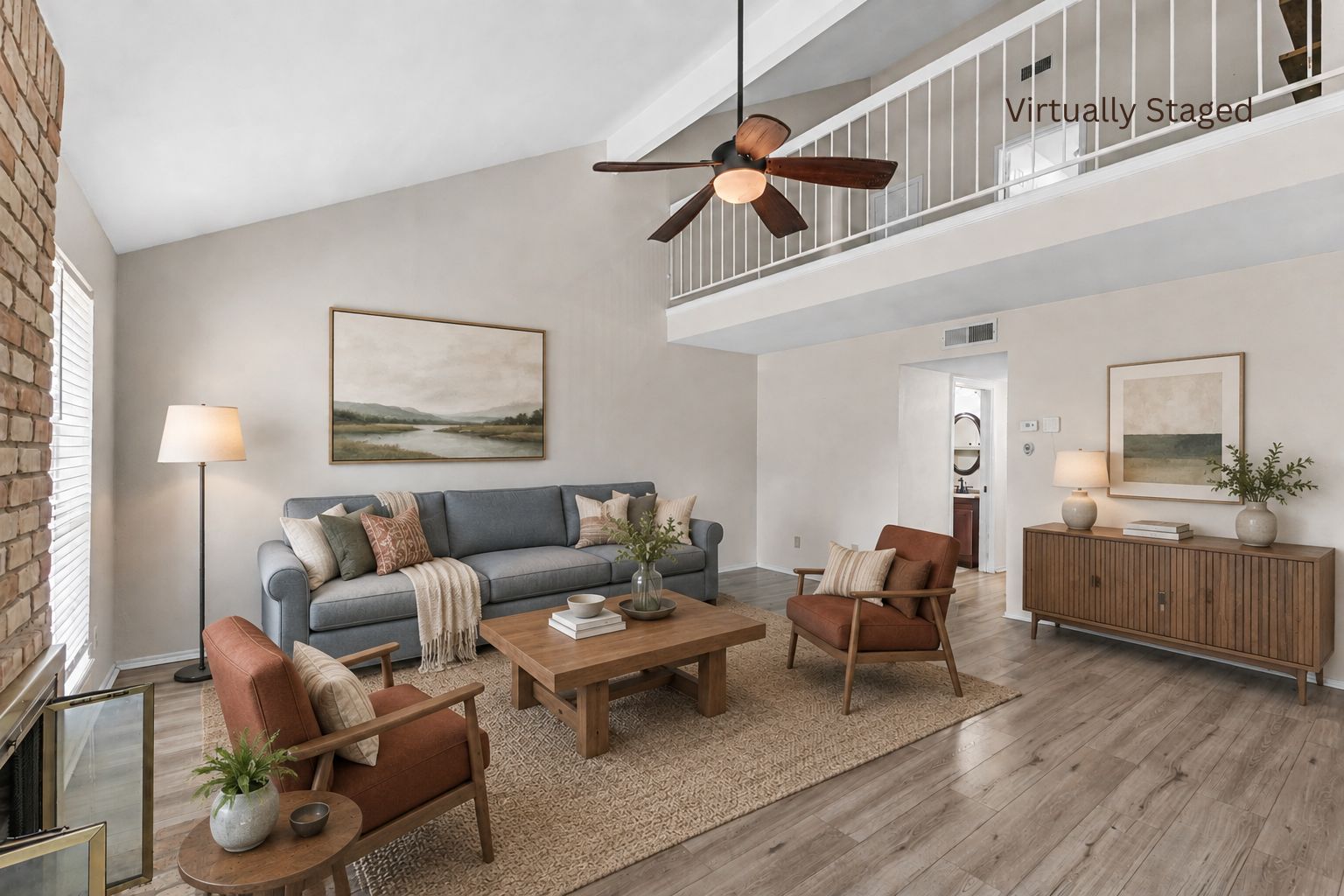Virtually staged living room with vaulted ceiling, brick fireplace, ceiling fan, and open loft above at 2100 Kippling Drive.